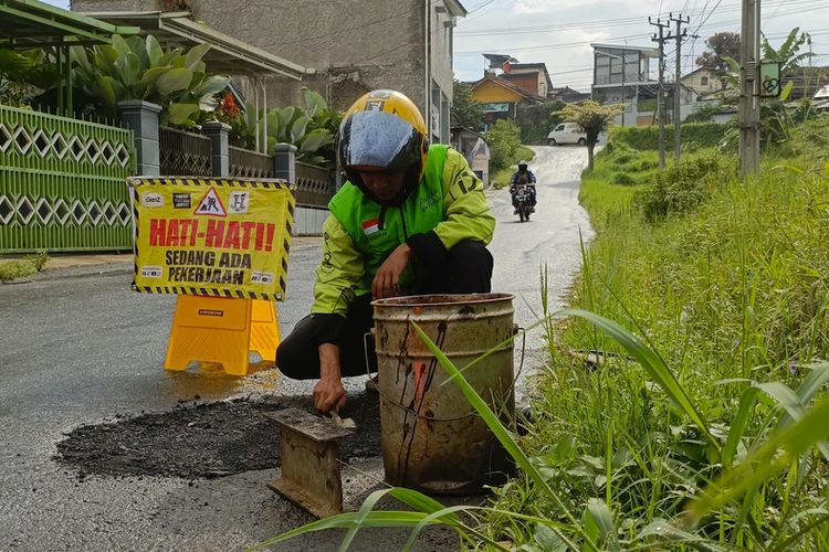 Hasan Fiidel (24) driver ojek online saat menambal salah satu jalan berlubang di Kecamatan Ciwidey, Kabupaten Bandung, Jawa Barat, Minggu (18/5/2025).