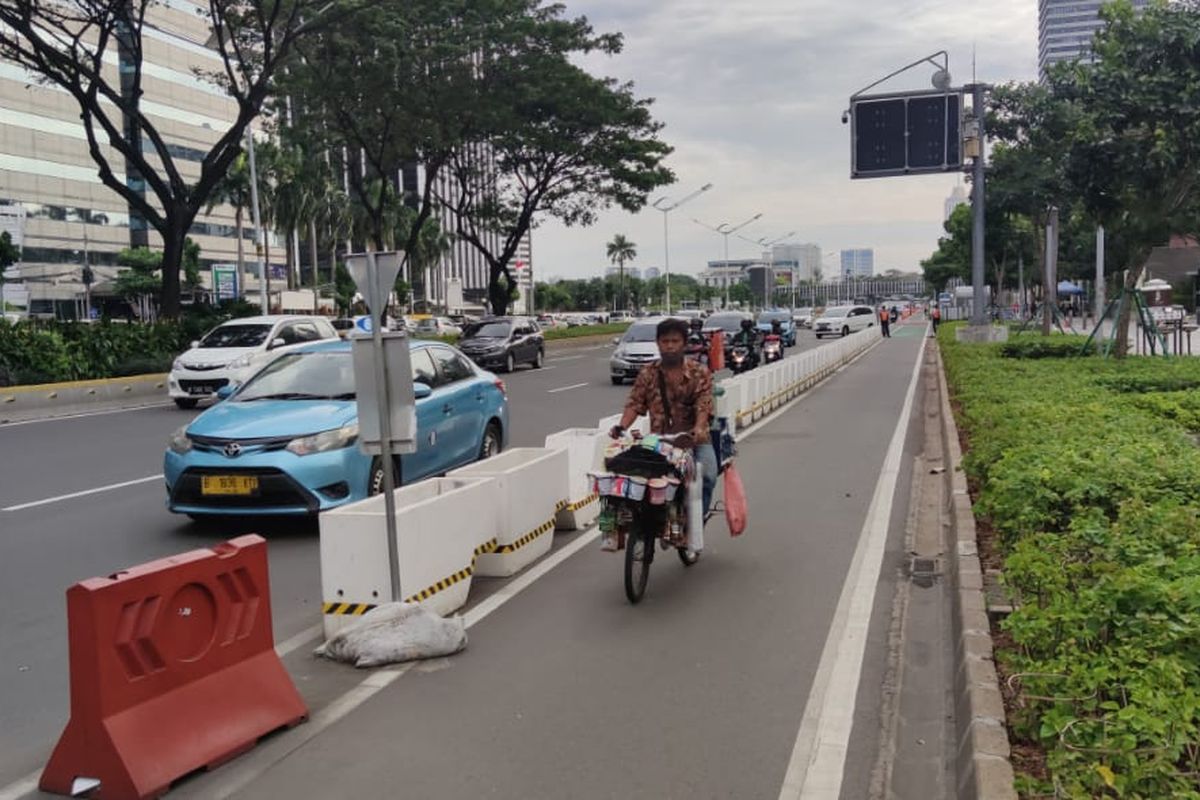 Pedagang kopi keliling, Jaelani (41) melintasi jalur sepeda permanen di Jalan Sudirman, Jakarta, Kamis (17/6/2021).