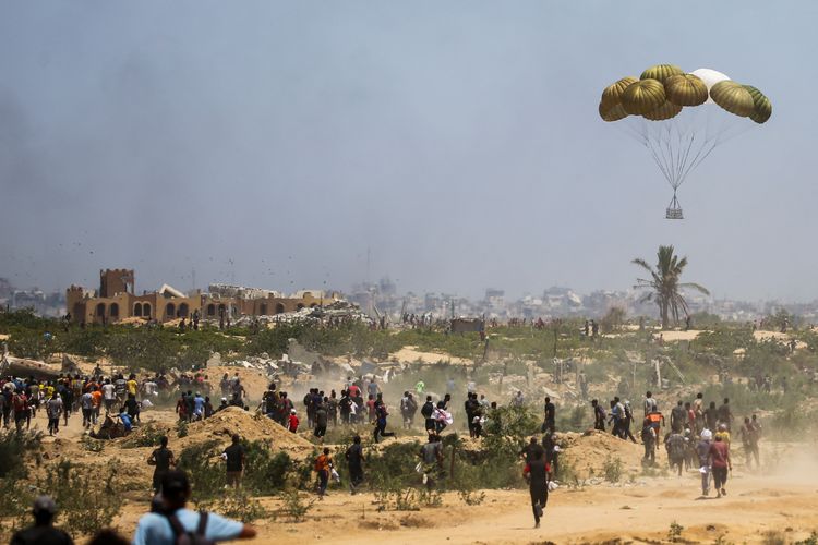 Gambar warga Palestina bergegas mengambil paket bantuan kemanusiaan yang diterjunkan di atas Nuseirat di Jalur Gaza tengah pada 6 Agustus 2025. Otoritas Gaza mendesak untuk setop kirim bantuan kemanusiaan via udara karena memperburuk krisis kemanusiaan dan menambah korban jiwa, tapi minta buka semua titik perbatasan di darat.