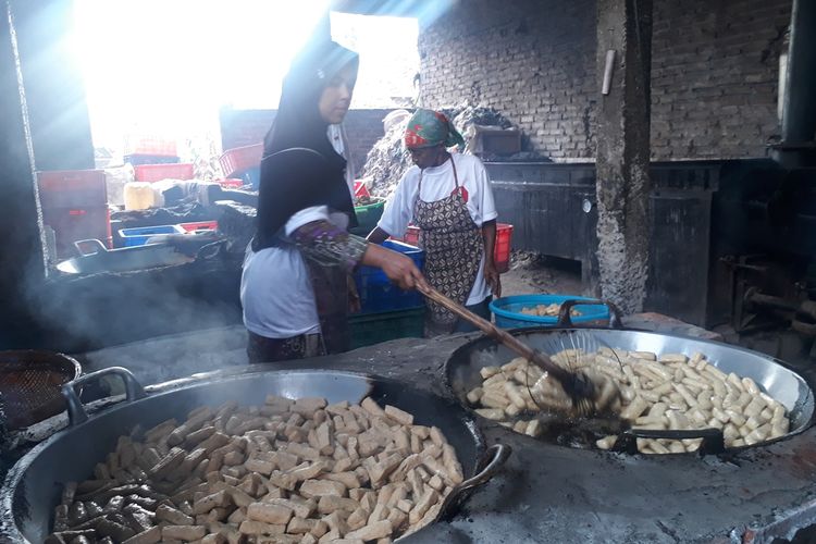 Dua orang pekerja sedang menggoreng tahu menggunakan limbah plastik impor dan oli bekas untuk perapian di salah satu pabrik penggorengan tahu di Desa Tropodo, Kecamatan Krian, Sidoarjo, Jawa Timur, Selasa (26/11/2019).