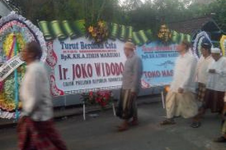 Pelayat melintas di depan karangan bunga dari Jokowi yang terpasang di dekat rumah duka KH Idris Marzuki, pengasuh pesantren Lirboyo, Kediri, Jawa Timur, Senin (9/6/2014).