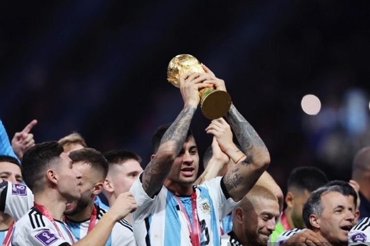 Bek timnas Argentina, Cristian Romero (tengah), mengangkat trofi Piala Dunia 2022 di Lusail Stadium setelah membantu timnya mengalahkan Perancis pada Minggu (18/12/2022). Terdekat, Romero dipastikan absen ketika Tottenham Hotspur menghadapi Brentford. Duel Brentford vs Tottenham merupakan laga pembuka Boxing Day Liga Inggris yang akan dihelat pada Senin (26/12/2022) malam WIB.