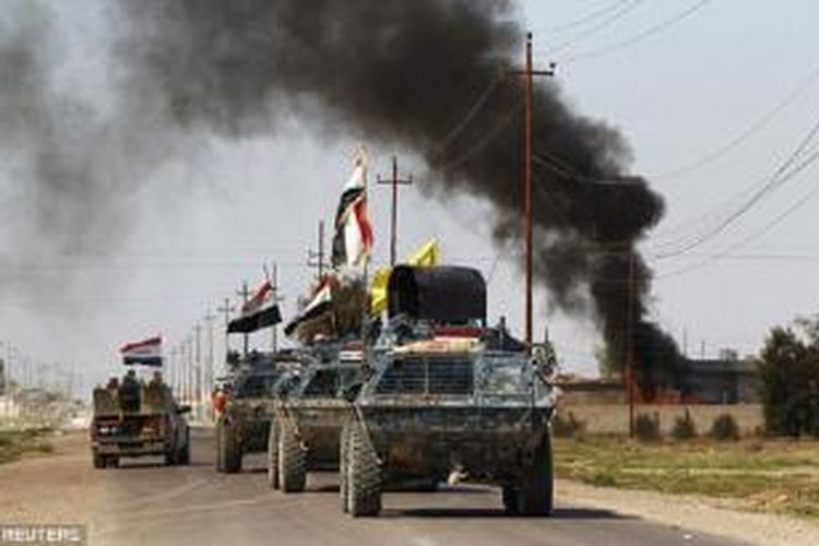 Kendaraan lapis baja pasukan keamanan Irak melewati asap hitam menyusul bentrokan dengan ISIS di Tikrit