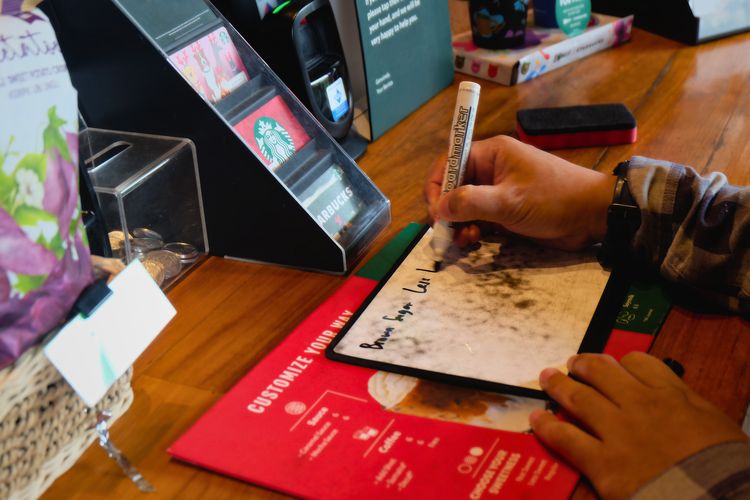 Salah satu pelanggan memesan minuman lewat papan tulis. Cara ini menjadi jembatan komunikasi antara barista Tuli dan pelanggan. Di sela-sela, barista Tuli biasa mengajarkan bahasa isyarat sederhana, seperti ?terima kasih? dan ?sama-sama?. 