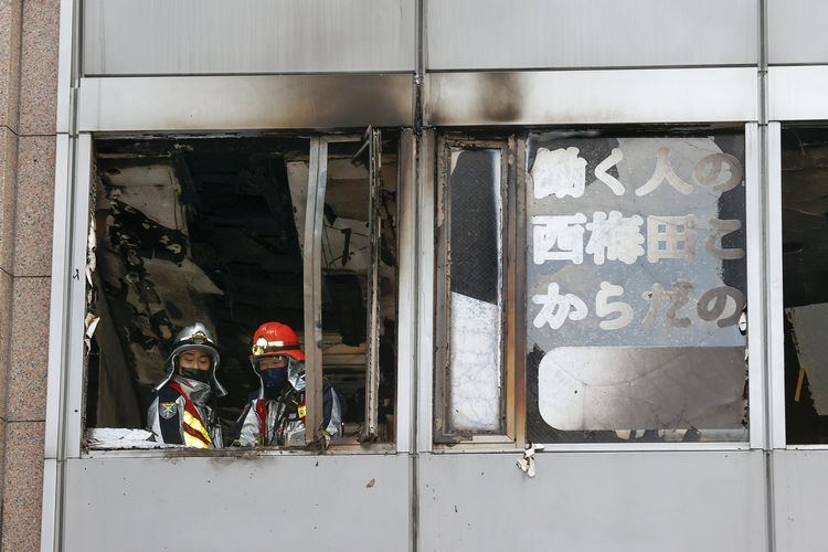 Petugas pemadam kebakaran berdiri di lokasi yang terbakar di gedung komersial di Osaka, Jepang, Jumat (17/12/2021). Kantor berita NHK melaporkan, puluhan orang dikhawatirkan tewas dalam kebakaran ini.