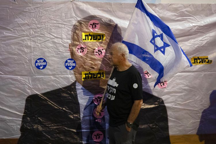 Seorang pengunjuk rasa Israel memegang bendera saat ia berjalan melewati spanduk yang menunjukkan Perdana Menteri Israel Benjamin Netanyahu (Tulisan berbahasa Ibrani artinya: Anda gagal dan Pergi), selama demonstrasi di luar kediaman Perdana Menteri di Yerusalem, Sabtu, 5 Juni 2021. 