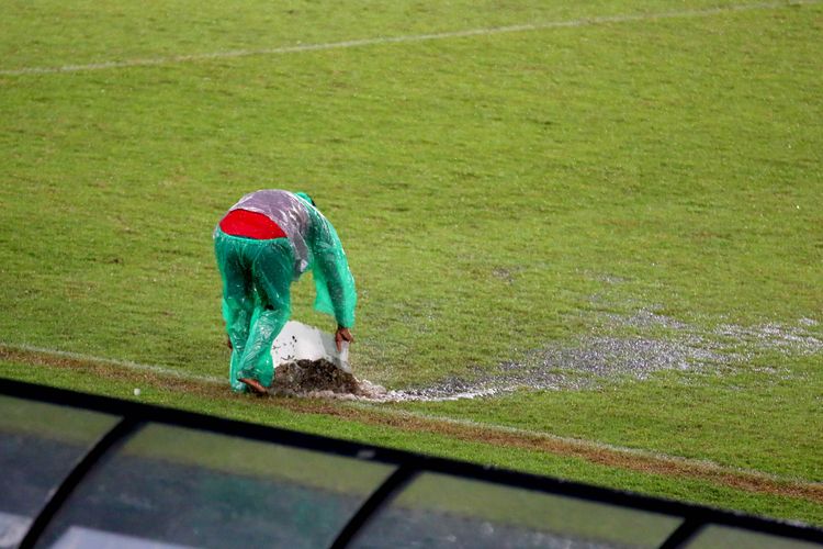 Seorang petugas sedang menyapu air tendangan dilapangan akibat hujan deras saat berlangsungnya pertandingan pekan ke-17 Liga 1 2022-2023 antara PSS Sleman melawan Persija Jakarta di Stadion Manahan Solo, Jumat (23/12/2022) sore.