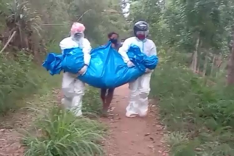 A screen shot of a video showing two officers and a middle-aged woman carrying the body of a Covid-19 patient wrapped in a tarpaulin in Ende Regency, East Nusa Tenggara.