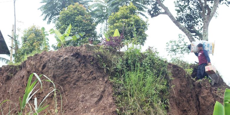 Seorang warga melintasi tebing yang longsor di Kampung Sindanglangu, Desa Batulawang, Kecamatan Cipanas, Kabupaten Cianjur, Jawa Barat akibat pergerakan tanah. 
