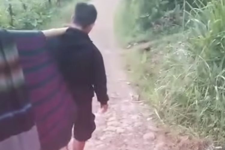 Tangkapan layar video viral Seorang warga sakit di Kampung Buah Batu, Desa Sukasari, Kecamatan Gununghalu, Kabupaten Bandung Barat (KBB), Jawa Barar terpaksa ditandu dengan sarung dan bambu sejauh lebih dari satu kilometer karena ambulans tidak mampu mencapai rumahnya, Selasa (2/12/2025).