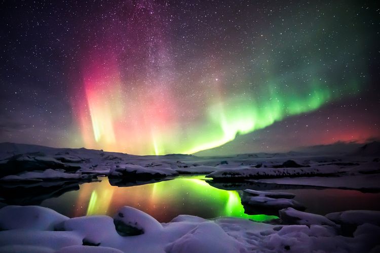 Gambar aurora berwarna merah dan hijau. Foto ini diambil di laguna Jokulsarlon, Islandia. Fenomena aurora adalah kilau cahaya warna-warni yang terbentuk karena adanya badai Matahari dan hanya terlihat di lingkaran Arktik dan Antartika.