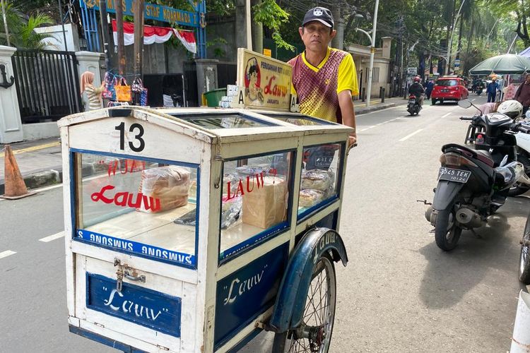 Pedagang roti Lauw menjajakan dagangannya dengan berkeliling menggunakan gerobak bertuliskan Lauw. 