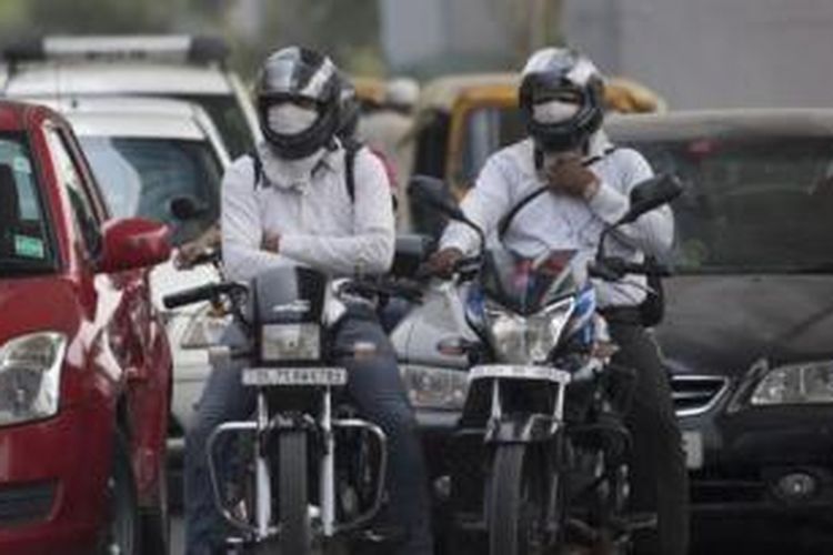 Pengendara motor menggunakan masker saat mengendarai kendaraannya melintasi jalanan kota New Delhi, India.