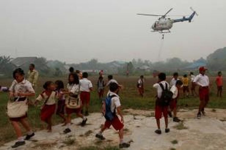 Murid Sekolah Dasar melihat helikopter Bolkow BO-105 milik Badan Nasional Penanggulangan Bencana (BNPB) yang akan melakukan pemadaman dengan teknik bom air (water bombing) di Desa Pelita Jaya, Kecamatan Kubu, Kabupaten Kubu Raya, Kalimantan Barat, Rabu (21/10/2015).