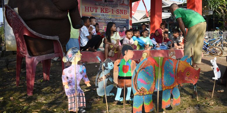 This picture taken on June 19, 2022 shows former teacher Samsudin (R) teaching children about animal conservation with cardboard puppets at Cemara Kulon village, in Indramayu. Samsudin is educating the young about the plight of the critically endangered Javan rhino - the world's rarest - with puppets on a stick, comical expressions and exaggerated voices, spreading his message of conservation one story at a time. TIMUR MATAHARI / AFP