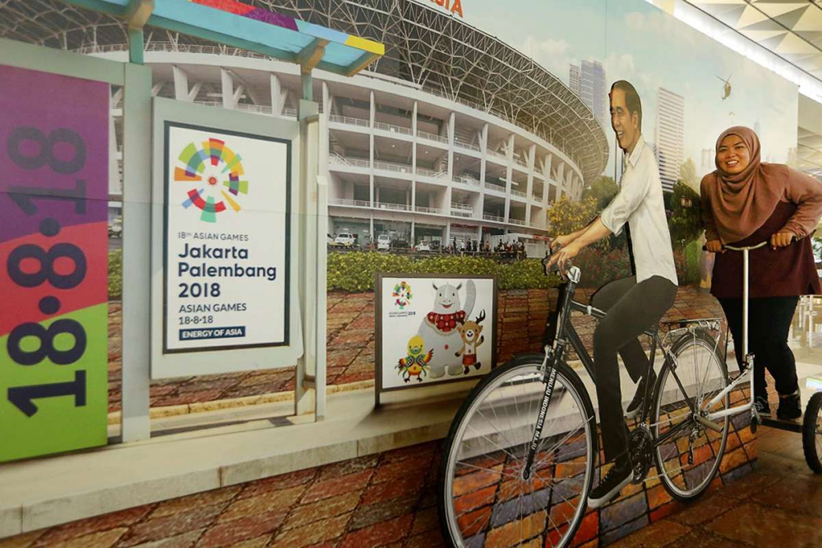 Seorang penumpang tengah berpose dengan foto Jokowi dan hiasan bertuliskan Asian Games 2018 di Terminal 3 Keberangkatan Bandara SOekarno-Hatta, Tangerang, Banten, Kamis (5/07/2018). PT Angkasa Pura AP (II) selaku pengelola bandara menyatakan siap memfasilitasi kedatangan dan kepulangan peserta Asian Games 2018 dengan menyiapkan sarana dan prasarana di tiga bandara yakni Bandara Soekarno Hatta, Bandara Sultan Mahmud Badaruddin II Palembang dan Husein Sastranegara Bandung.