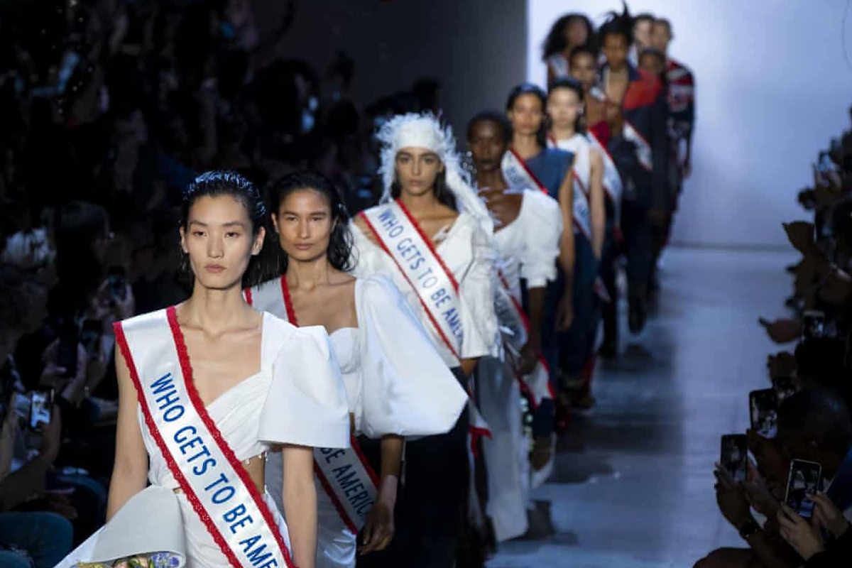 Model memakai selempang bertuliskan Who gets to be American dalam peragaan busana Prabal Gurung.