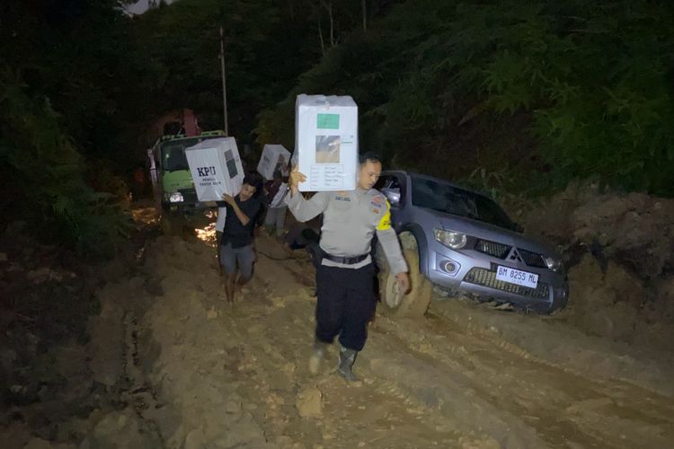 Petugas kepolisian memikul logistik pemilu melewati jalan rusak dan berlumpur menuju Desa Cipang Kiri Hulu, Kecamatan Rokan IV Koto, Kabupaten Rokan Hulu, Riau, Senin (12/2/2024) malam.