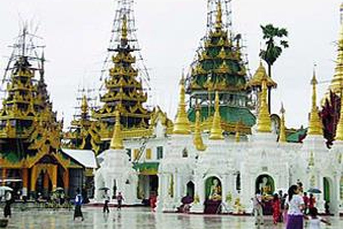 Beberapa pengunjung melintas di depan stupa di kompleks Pagoda Shwedagon, Yangon, Myanmar, yang tengah diperbaiki, akhir Juni lalu. 