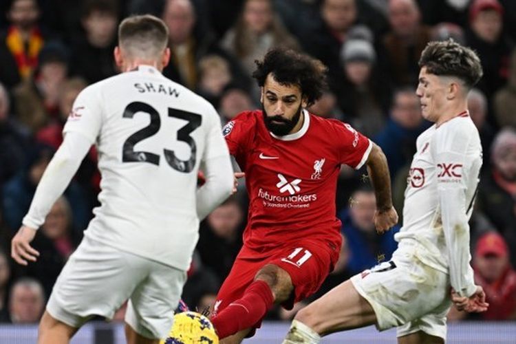 Pemain sayap Liverpool, Mohamed Salah (tengah), melepaskan umpan di antara penjagaan dua pemain Manchester United, Luke Shaw dan Alejandro Garnacho. Laga Liverpool vs Man United pada pekan ke-17 Liga Inggris 2023-2024 tersebut digelar di Stadion Anfield, Minggu (17/12/2023). (Foto oleh PAUL ELLIS/AFP)