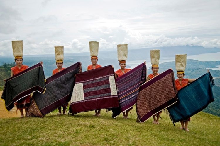 Para wanita mengenakan pakaian adat Sumatera Utara dan membentangkan kain Ulos khas Batak.