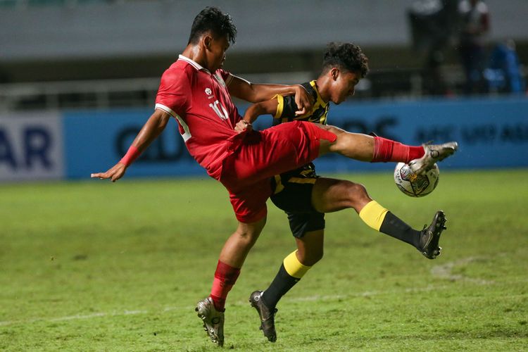 Pemain timnas U17 Indonesia Muhammad Nabil Asyura berebut bola dengan pemain timnas Malaysia Danish Darus pada laga Kualifikasi Piala Asia U17 2023 di Stadion Pakansari, Kabupaten Bogor, Minggu (9/10/2022).