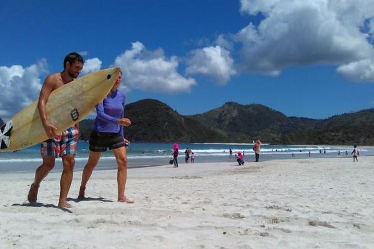 Wisatawan asing berjalan di Pantai Selong Belanak usai berselancar.