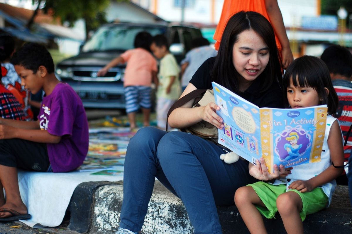 Seorang relawan dari Komunitas Tanah Ombak sedang mengajar membaca kepada anak-anak di kawasan Sebrang Pabayan, tepi Sungai Batang Arau, Padang, Sumatera Barat, Minggu (16/7/2017). Tanah Ombak meluncurkan kegiatan pustaka bergerak yang diberi nama Vespa Pustaka untuk menjangkau anak-anak di Kota Padang yang membutuhkan akses pendidikan lewat buku bacaan.