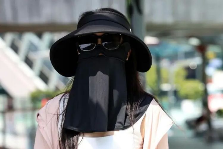 Seorang turis China mengenakan topi, kacamata hitam, dan penutup wajah untuk melindungi diri dari sinar matahari saat gelombang panas di Bangkok, Thailand, pada 1 April 2024.