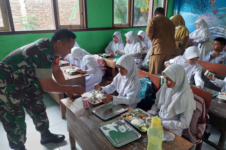 Babinsa Kodim 0813 Bojonegoro saat mengawal proses pendistribusian makan siang gratis kepada para siswa di Kabupaten Bojonegoro, Jawa Timur oleh Satuan Pelayanan Pemenuhan Gizi (SPPG) di SD Negeri Sumbang, Bojonegoro, Senin (6/1/2025).