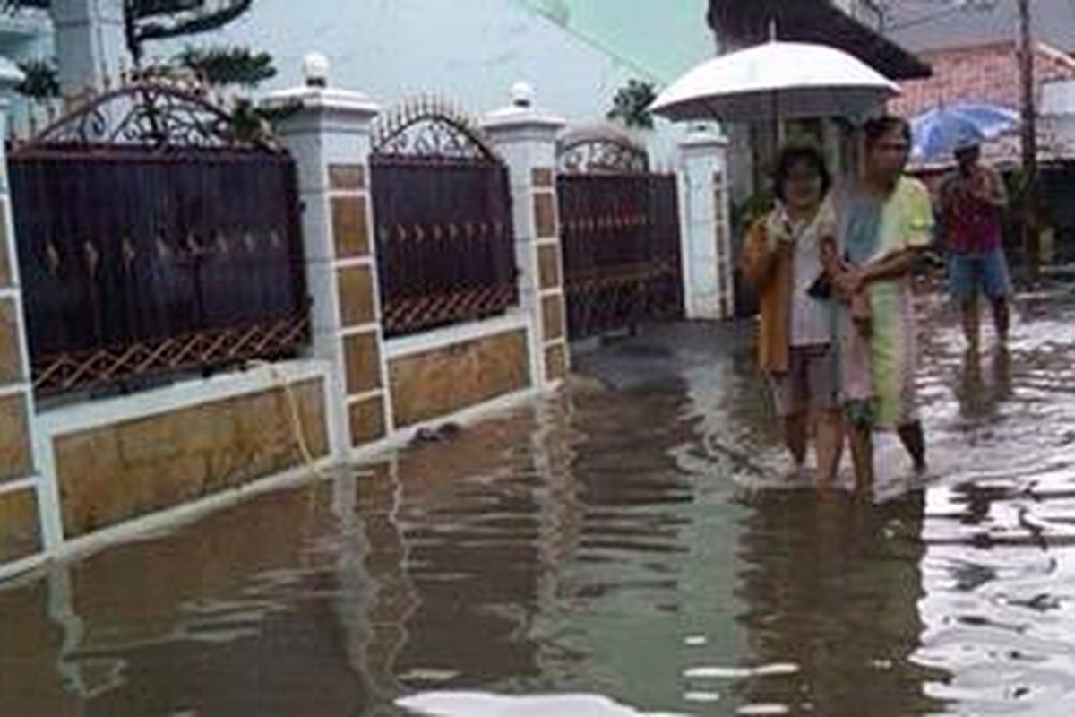 Dua orang warga RT 10 RW 08 Kampung Gedong, Pasar Rebo, Jakarta Timur, tampak tengah berjalan di antara genangan banjir.