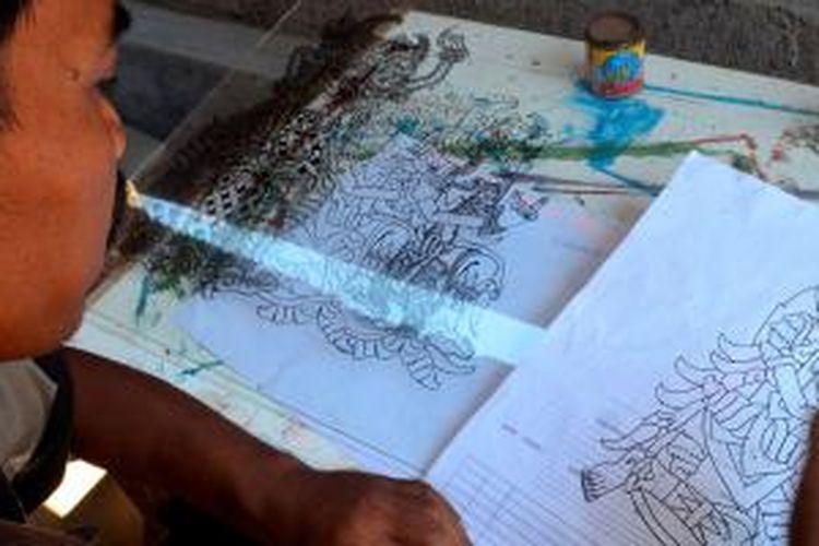 I Ketut Santosa sedang membuat sketsa wayang di atas kertas sebagai tahap awal melukis kaca nagasepaha.