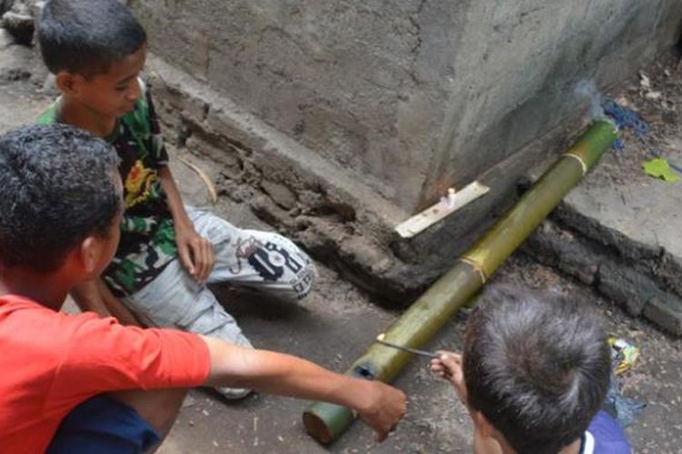 Tiga orang anak sekolah dasar di Kompleks Mabako, Kelurahan Watunggene, Kecamatan Kota Komba, Manggarai Timur, Flores, NTT, Jumat (19/12/2014) membunyikan meriam bambu di samping rumah mereka. Tradisi meriam bambu merupakan warisan leluhur orang Flores untuk menyambut kelahiran Isa Almasih.  