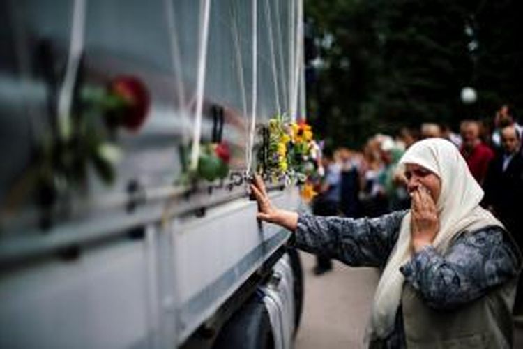 Seorang perempuan Bosnia menangis saat menyentuh bak sebuah truk yang membawa  peti berisi jasad korban pembantaian Srebrenica yang baru diketahui identitasnya di kota Visoko, dekat Sarajevo.