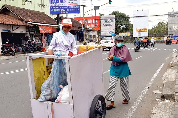 Sri Subekti saat mendorong gerobak berkeliling mencari rongsokan untuk dijual. Tampak Sri Subekti ditemani anaknya Nisabela putri yang baru berusia 10 tahun.