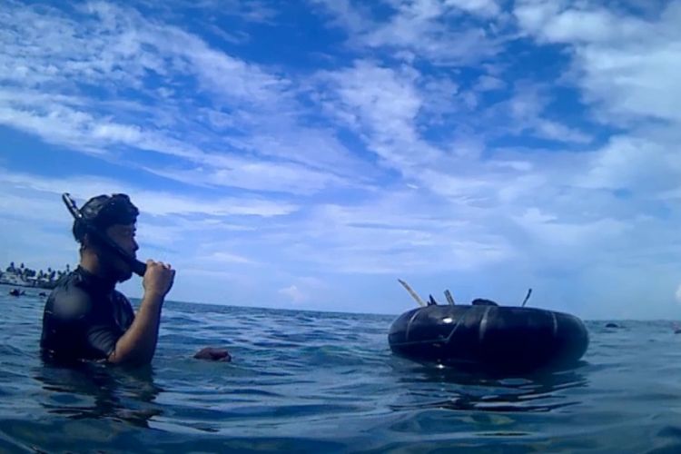 David Wong dengan membawa karet ban yang di bawahnya terdapat jaring sebagai tempat mengumpulkan sampah yang ada di laut di kawasan Museum Pusaka Nias, Kepulauan Nias, Sumatera Utara.