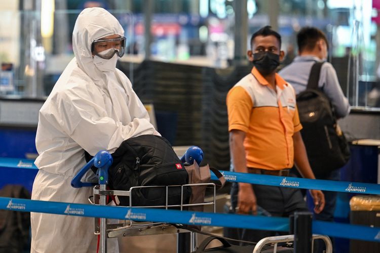 Seorang penumpang (kiri) memakai pakaian APD saat mengantre untuk check-in penerbangan di Kuala Lumpur International Airport (KLIA), Sepang, Malaysia, 29 November 2021.