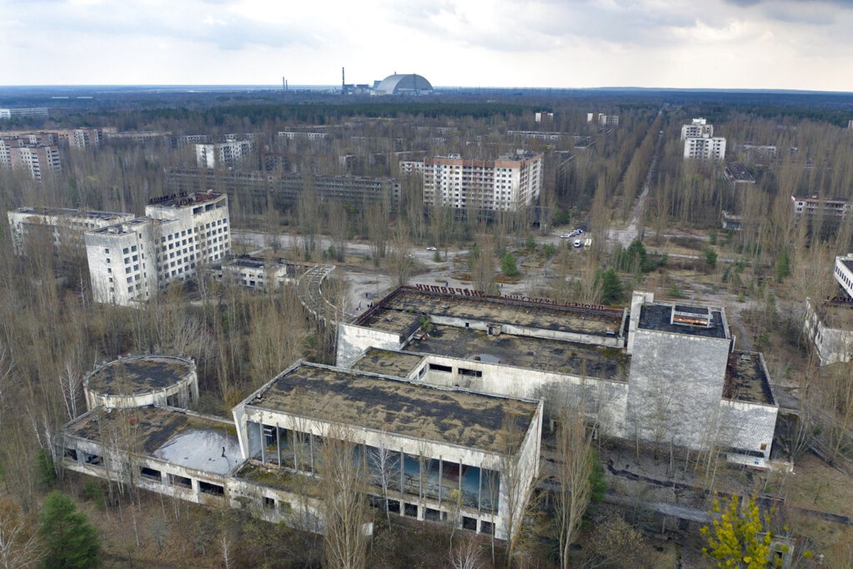 Pemandangan kota hantu Pripyat dengan tempat perlindungan yang menutupi reaktor yang meledak di pembangkit nuklir Chernobyl di latar belakang, Ukraina, Kamis, 15 April 2021. 