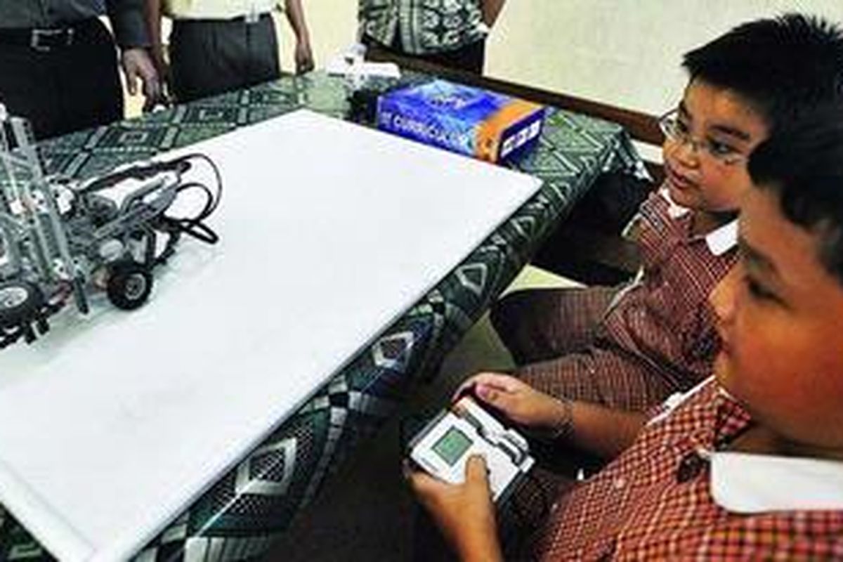 Dua siswa mencoba menjalankan robot yang dapat memindahkan benda, Rabu (17/3), di Sekolah Dasar YPPI 1, Surabaya. Robot sebagai salah satu media belajar terutama pada pelajaran Matematika, Fisika dan pengenalan mekanik telah banyak diminati sekolah dengan memasukkan ke dalam pelajaran ekstrakurikuler ataupun intrakurikuler.