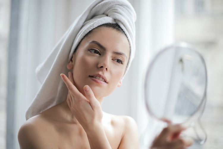 Ilustrasi perempuan dengan kulit glowing yang sedang menatap cermin.