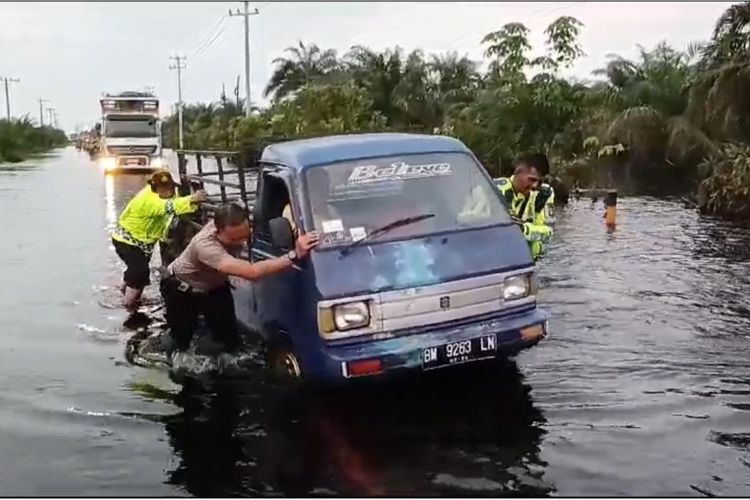 Petugas kepolisian saat mengevakuasi mobil yang mogok di tengah banjir di jalan lintas sumatera, di Kabupaten Pelalawan, Riau, Sabtu (27/1/2024).