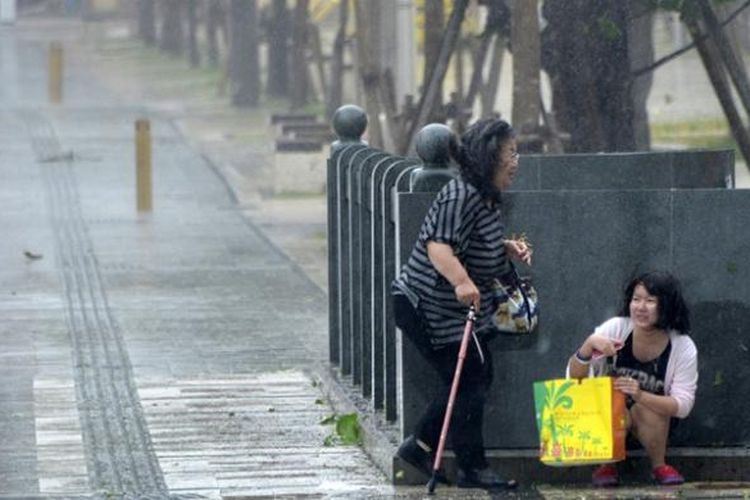 Ilustrasi : Dua perempuan warga kota Naha, Okinawa, Jepang berlindung dari terjangan badai
