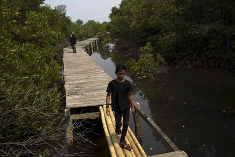 Warga berhati-hati melewati titian bambu di Jembatan Pelangi, Pulau Lancang, Kepulauan Seribu, Minggu (18/10/2015). Jembatan yang masih dalam proses pembangunan itu nantinya akan dibuat mengitari hutan bakau di bagian barat Pulau Lancang. 