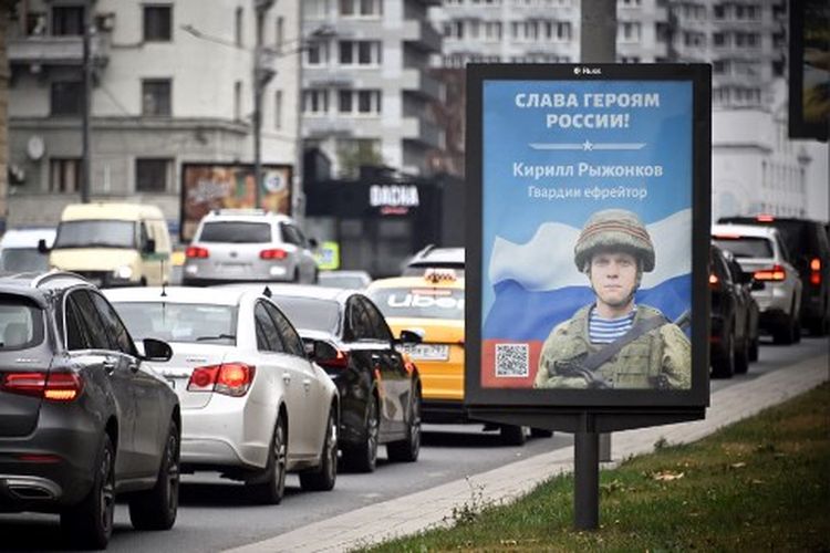 Mobil-mobil melewati papan reklame yang menampilkan Spesialis Airborn Rusia Kirill Ryzhonkov dengan slogan bertuliskan 'Glory to the Heroes of Russia' di Moskow tengah pada 28 September 2022.
