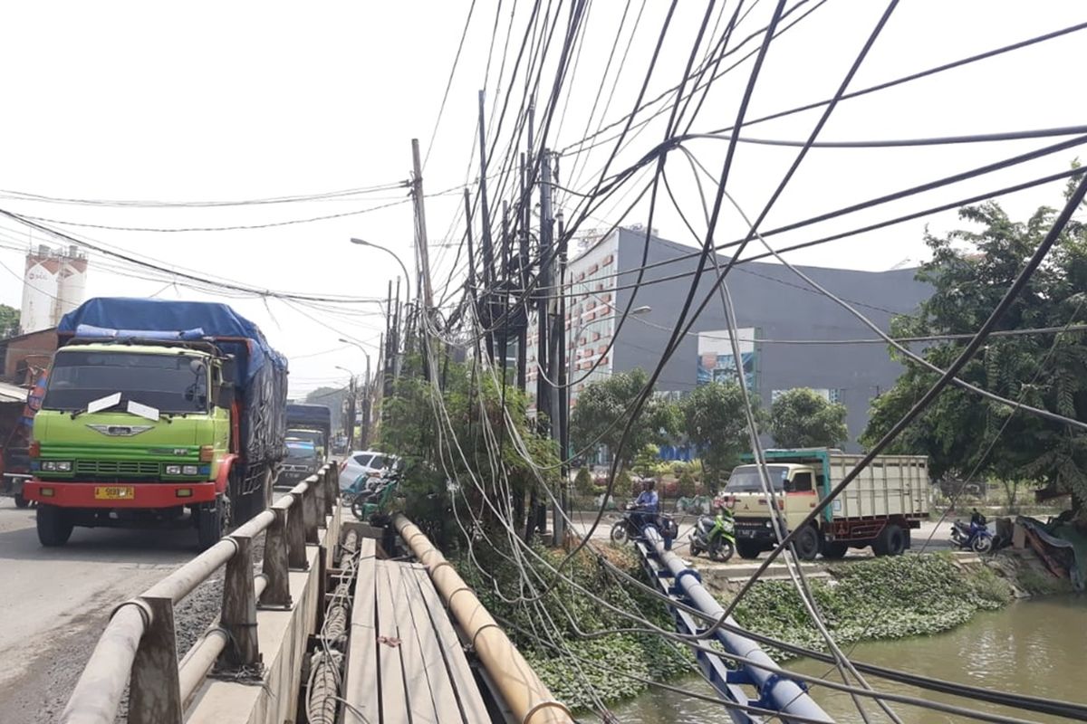 Setidaknya 13 tiang yang terdiri dari antara lain tiang untuk jaringan listrik, internet, dan telekomunikasi menancap di satu titik di Jalan Pejuang, dekat kawasan Grand Satria City, Medansatria, Kota Bekasi, Rabu (27/11/2019). Kabel-kabel yang terhubung dengan tiang-tiang tersebut beberapa tampak telah kendur sehingga membahayakan para pengendara yang melintas.