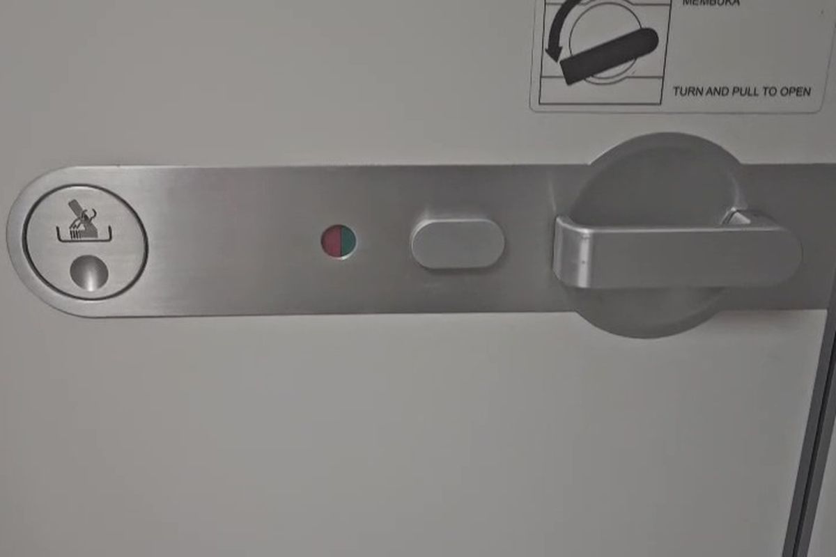 Tanda merah di pintu pesawat menandakan bahwa toilet sedang dipakai penumpang lain.