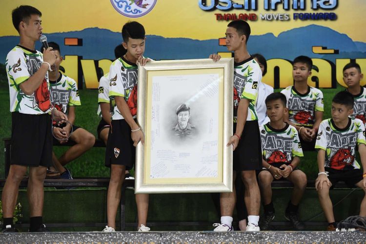 Pelatih sepak bola ''Wild Boars'' Ekkapol Chantawong (kiri) bersama 12 remaja yang berhasil diselamatkan setelah terjebak di goa di Thailand, memberikan penghargaan kepada relawan dan mantan penyelam Navy SEAL Thailand Saman Kunan yang tewas saat proses penyelamatan mereka.