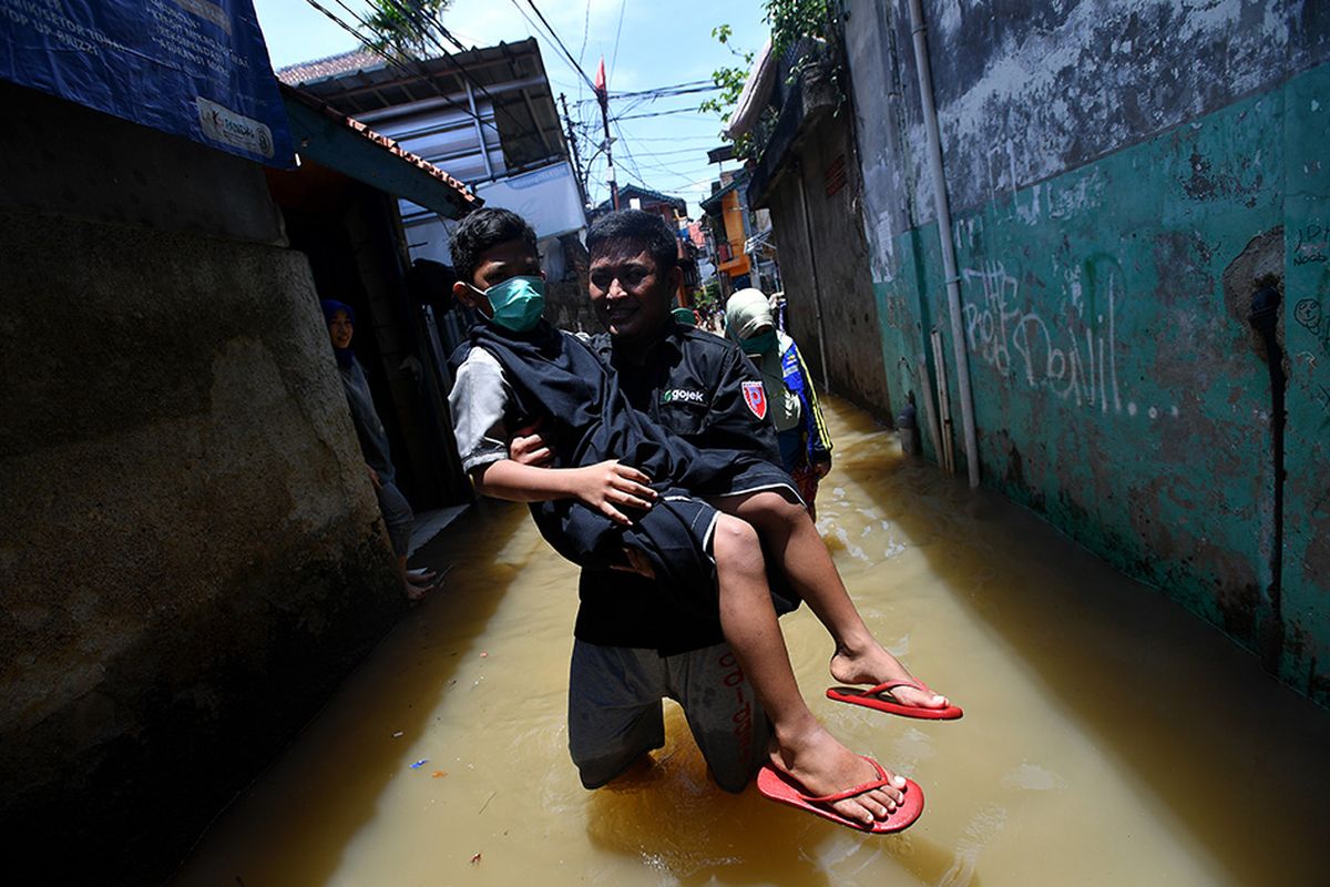 Seorang warga membawa anaknya yang baru selesai dikhitan melewati banjir di kawasan permukiman di Petogogan, Kebayoran Baru, Jakarta Selatan, Senin (5/10/2020). Banjir tersebut terjadi akibat meluapnya Kali Krukut.
