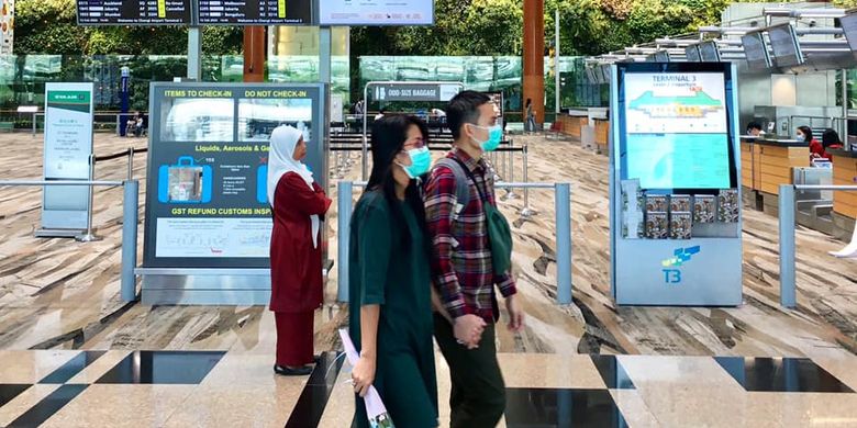 Pasangan muda-mudi terlihat memakai masker di Terminal 3 Bandara Internasional Changi di tengah mewabahnya virus corona di Singapura.  