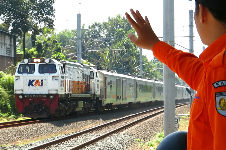 Petugas Penjaga Jalan Lintasan (PJL) melakukan semboyan dengan masinis kereta api.